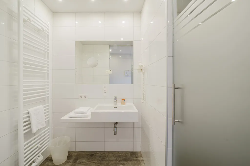 Badezimmer mit Glastür, Waschtisch und Handtuchheizkörper im Motel Baden