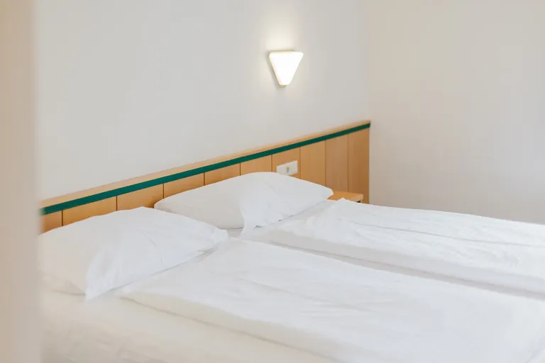 Frisch bezogenes Bett mit Wandleuchte im Motel Baden
