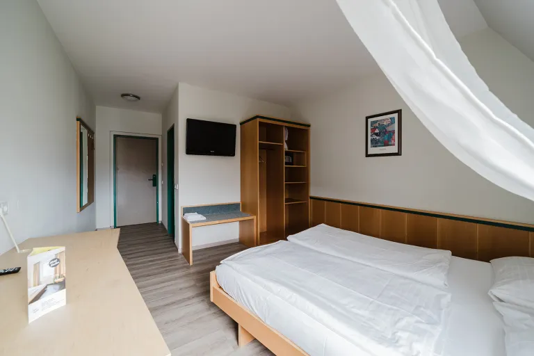 Doppelzimmer im Dachgeschoss mit Bett, Kasten und Flat-TV im Motel Baden