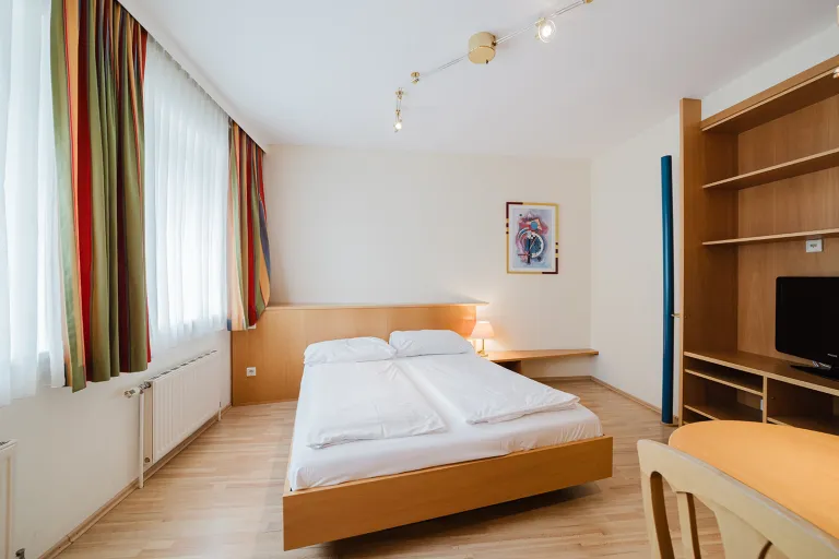 Doppelbett vor Fensterfront mit Regalwand und TV im Motel Baden