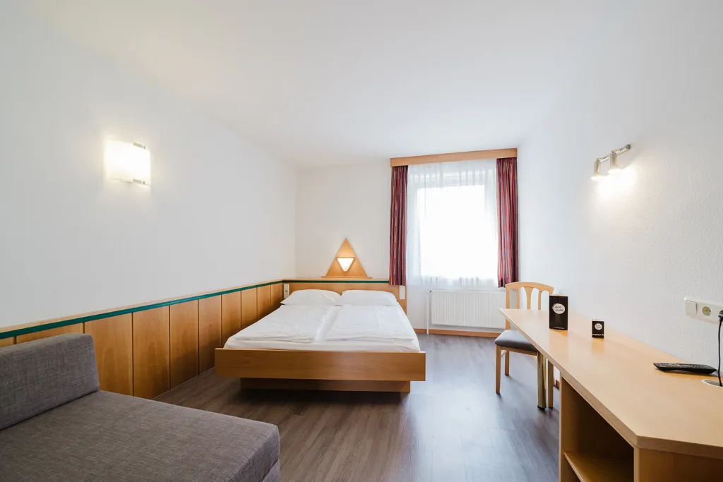 Zimmer über der Garage mit Doppelbett, Sitzecke und Schreibtisch im Motel Baden