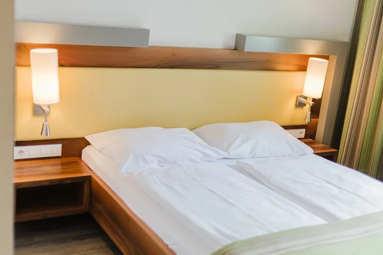 Doppelbett vor gelber Wand mit Leselampen im Motel Baden