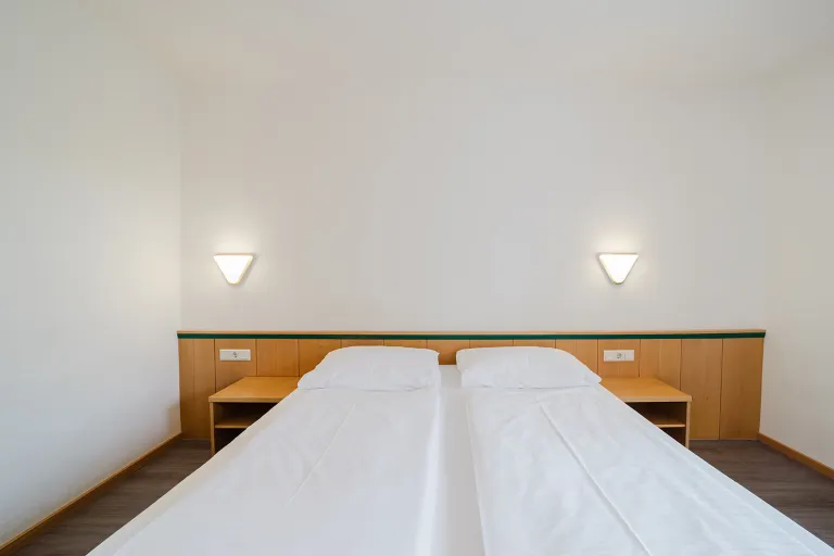 Modernes Doppelzimmer mit zwei zusammengestellten Betten und Wandleuchten im Motel Baden