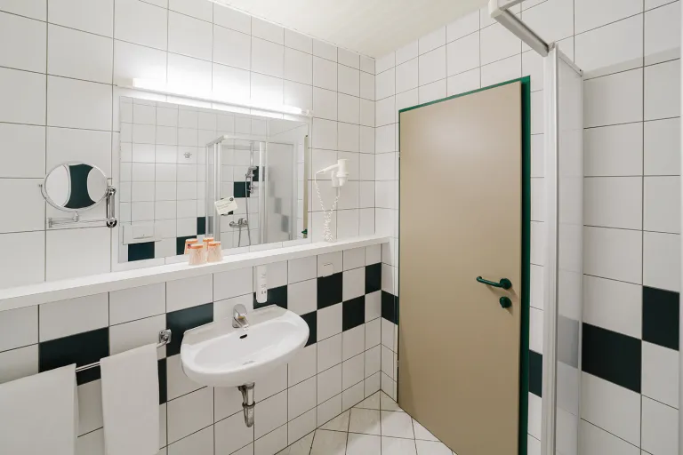 Waschtisch mit Spiegel im grün-weiß gefliesten Bad im Motel Baden